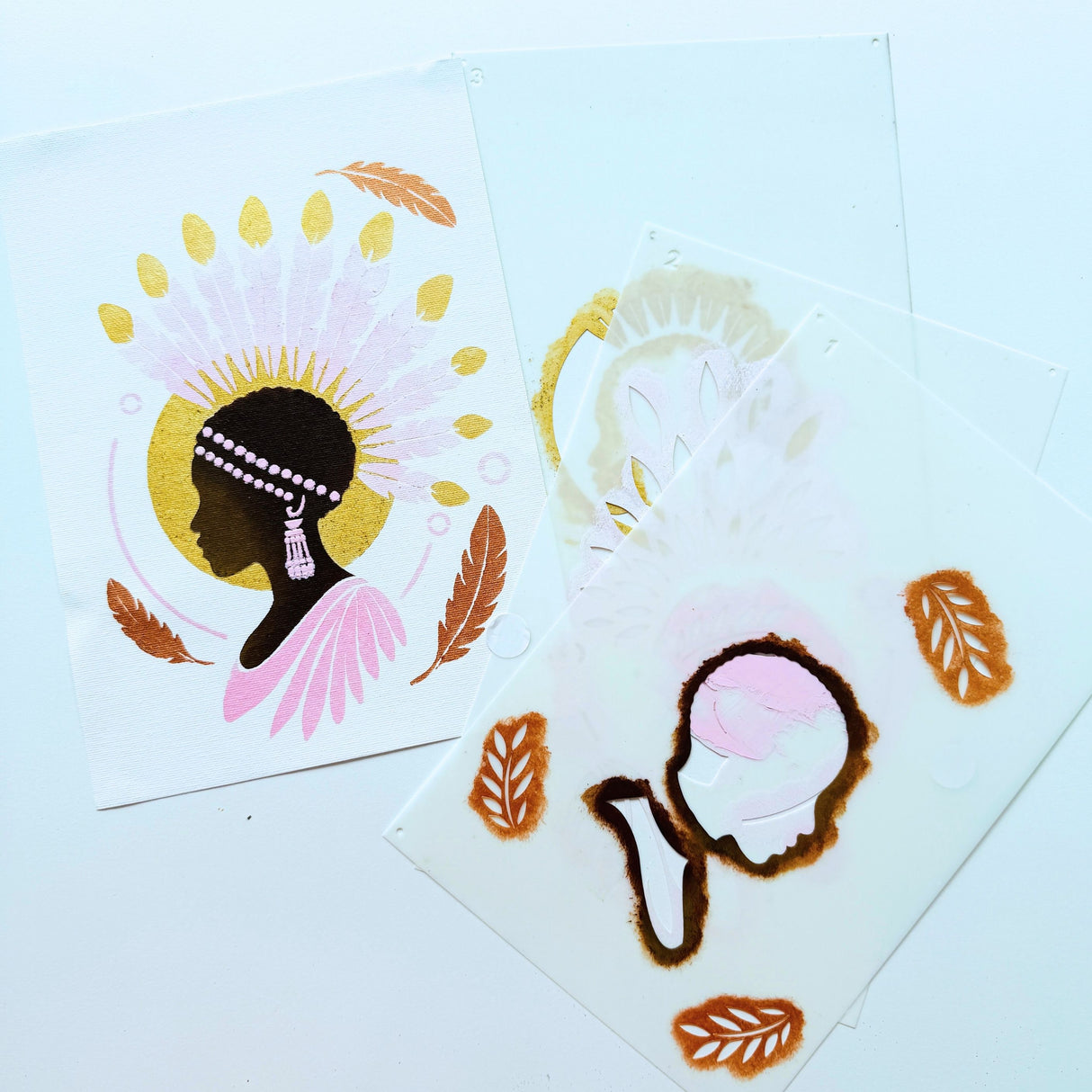 Les trois pochoirs superposables du modèle Crépuscule d’Amani, utilisés pour créer la silhouette et les plumes, présentés avec l’œuvre peinte finale.