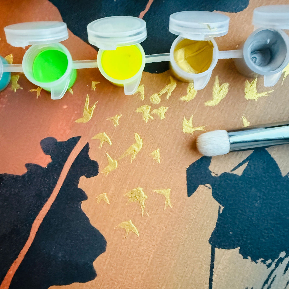 Détail du modèle Hanoï réalisé avec le pochoir artistique Panash Art.
On voit le pinceau, les godets de peinture jaune et or, et les oiseaux peints sur le fond coloré.