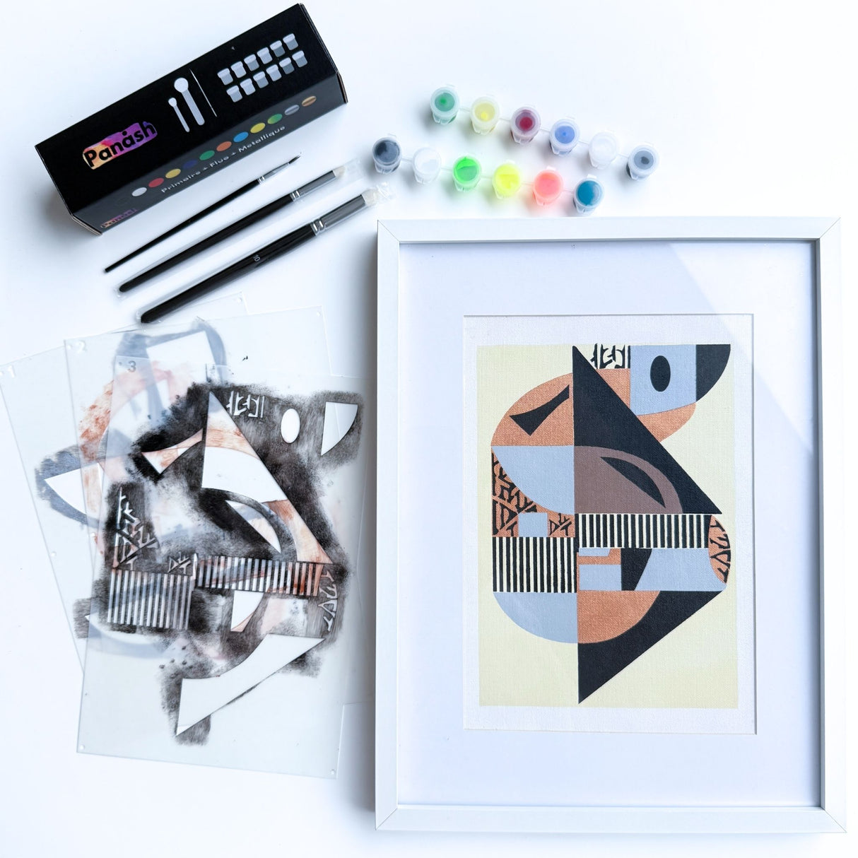 Kit pochoir artistique Panash Art modèle Absolu en trois superpositions, œuvre abstraite géométrique aux tons noir, ocre et bleu, avec cadre blanc, pinceaux et peintures incluses pour création DIY à la maison. Oeuvre murale diy, loisir créatif maison, décoration intérieure moderne